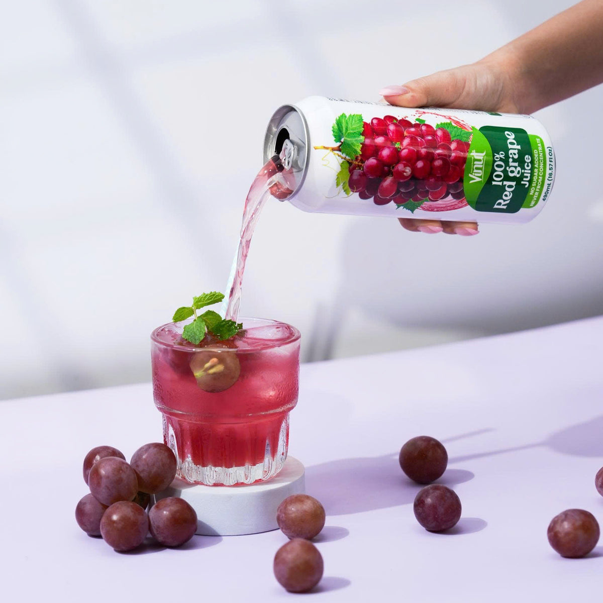 VINUT 100% grape juice can on table poured into glass with fresh tropical fruit
